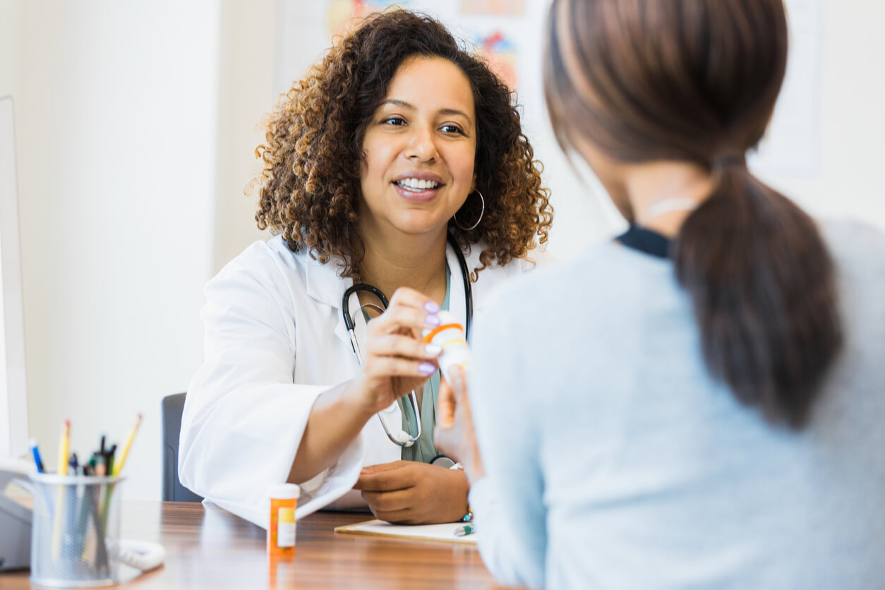 female doctor hands prescription bottle to unrecognizable female patient