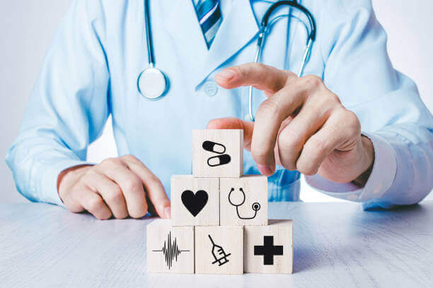 family doctor pointing on cubes stacked with medical icons - health concept