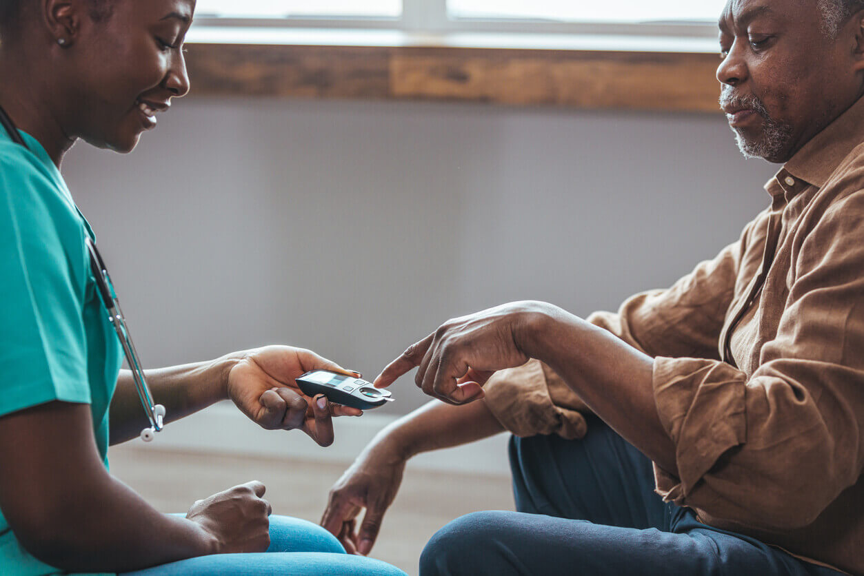A primary care physician supports a senior male patient with diabetes by measuring his blood glucose levels indoors.